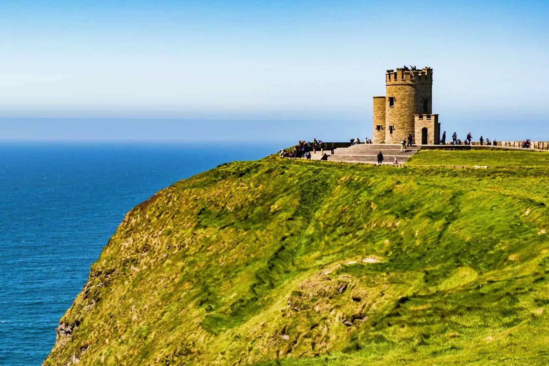 Historic stone tower overlooking the Atlantic Ocean on a green Irish cliff with visitors gathered at the base